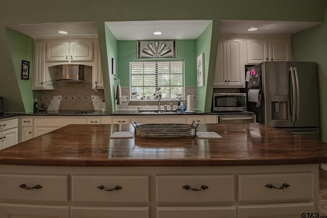 kitchen featuring white cabinetry, sink, wall chimney range hood, a kitchen island, and appliances with stainless steel finishes