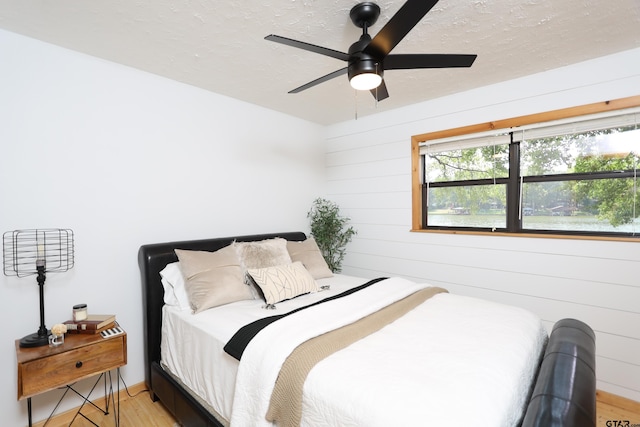 306 Lake Dr, Mount Vernon, TX 75457 - bedroom featuring a textured ceiling, light wood-style floors, wood walls, and ceiling fan