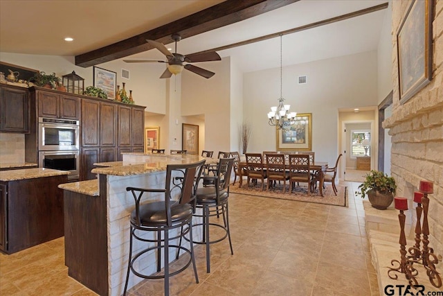 kitchen with light stone counters, dark brown cabinetry, double oven, pendant lighting, and a kitchen island