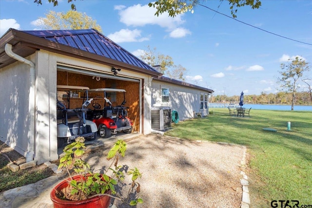 view of side of home with a yard, a water view, central AC unit, and an outdoor structure