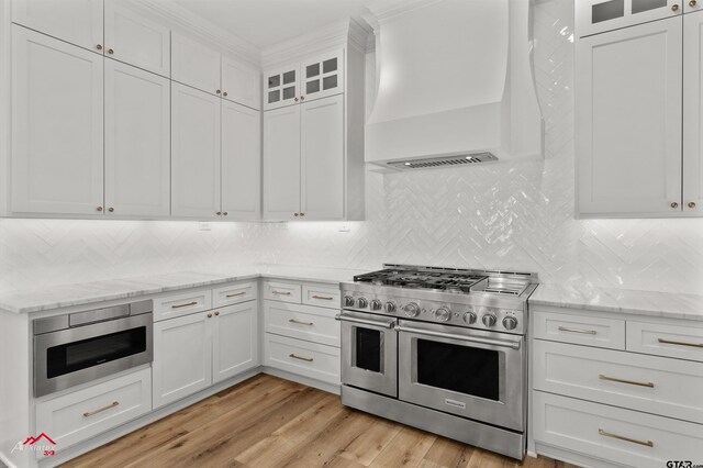 6309 Gleneagles, Tyler, TX 75703 - kitchen with light wood-style flooring, premium range hood, appliances with stainless steel finishes, white cabinetry, and backsplash