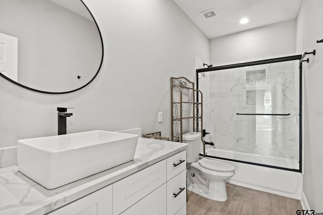 full bathroom with hardwood / wood-style flooring, vanity, combined bath / shower with glass door, and toilet