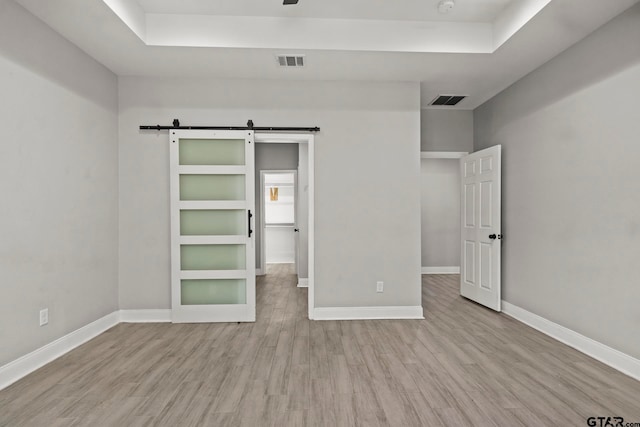 unfurnished bedroom featuring a barn door, a raised ceiling, and light wood-type flooring