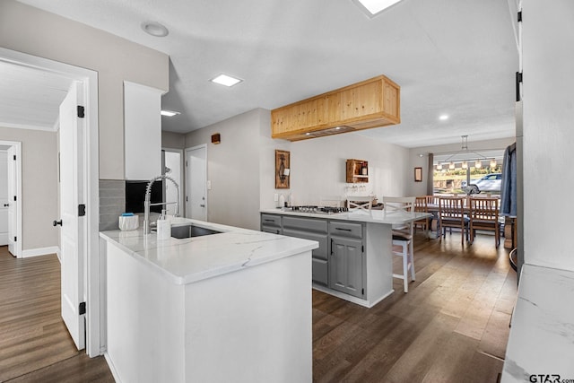 kitchen with kitchen peninsula, light stone counters, sink, gray cabinets, and a breakfast bar area