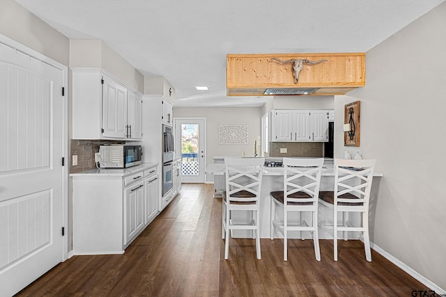 kitchen with kitchen peninsula, a kitchen breakfast bar, backsplash, and white cabinetry