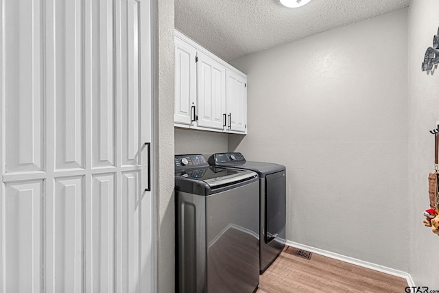 washroom featuring cabinets, a textured ceiling, light wood-type flooring, and washing machine and clothes dryer