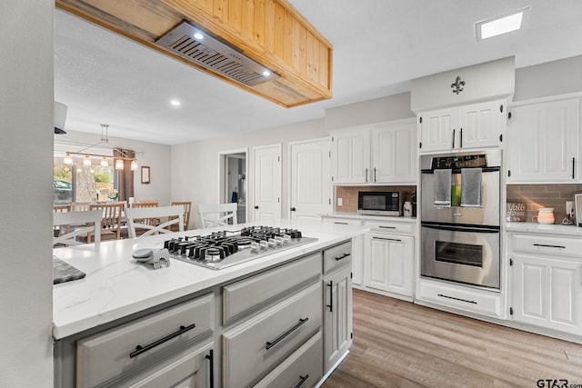 kitchen with decorative backsplash, white cabinets, light hardwood / wood-style floors, and appliances with stainless steel finishes