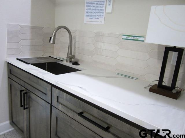 kitchen featuring dark brown cabinets, sink, backsplash, and light stone countertops