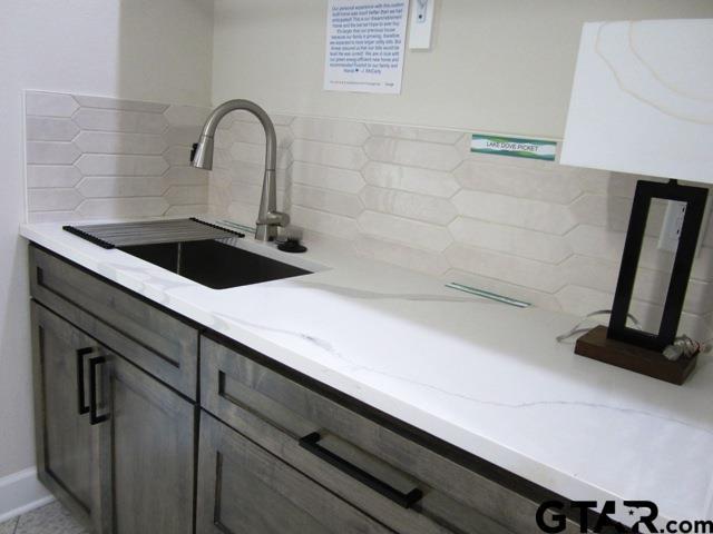 7924 Crooked Trl, Tyler, TX 75703 - kitchen featuring a sink, backsplash, light stone counters, and gray cabinets