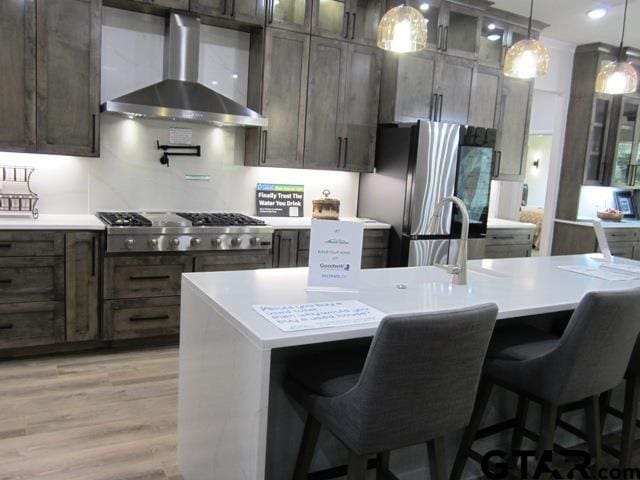 kitchen with hanging light fixtures, a kitchen bar, wall chimney exhaust hood, and appliances with stainless steel finishes