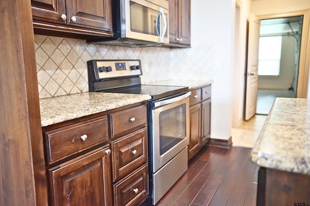 kitchen with dark brown cabinetry, light stone counters, appliances with stainless steel finishes, dark hardwood / wood-style floors, and backsplash