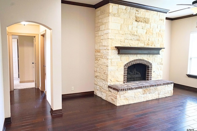 unfurnished living room featuring dark wood-type flooring, ceiling fan, a stone fireplace, and ornamental molding