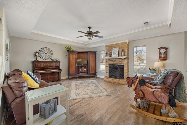 living room with ceiling fan, a fireplace, light hardwood / wood-style floors, a raised ceiling, and a textured ceiling