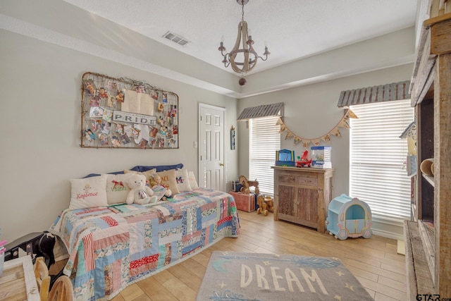 bedroom with multiple windows, light hardwood / wood-style flooring, a textured ceiling, and a chandelier