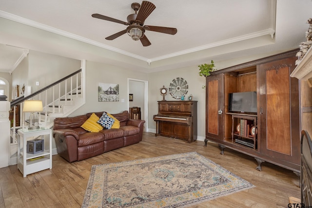 living room with light wood-type flooring, ceiling fan, ornamental molding, and a tray ceiling