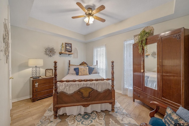 bedroom with a raised ceiling, ceiling fan, and light wood-type flooring