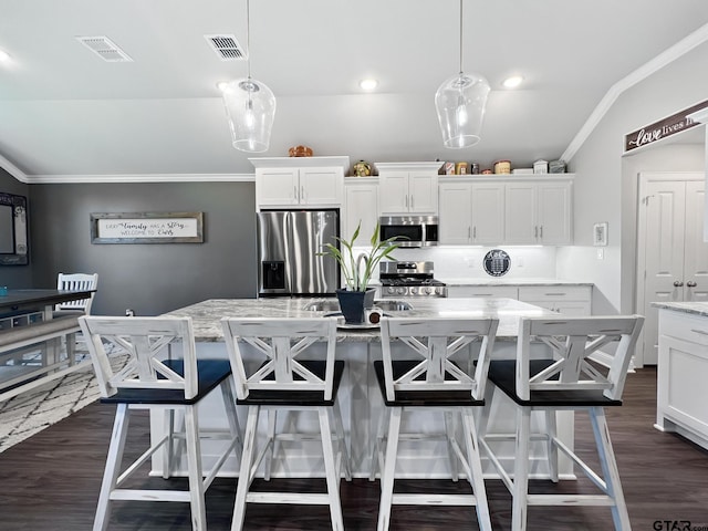 kitchen featuring hanging light fixtures, appliances with stainless steel finishes, a kitchen island, a kitchen bar, and white cabinetry