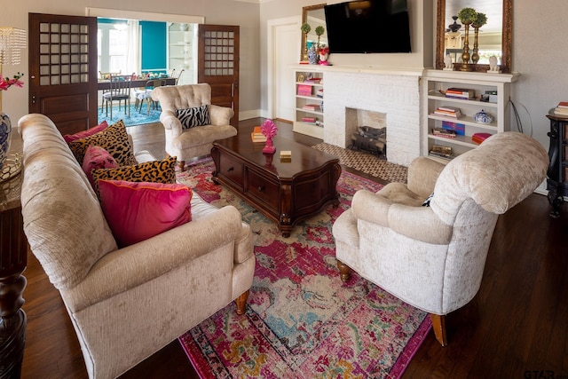 living room featuring a brick fireplace, baseboards, and wood finished floors