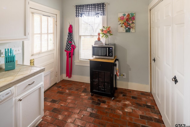 interior space featuring tile countertops, stainless steel microwave, white dishwasher, and baseboards