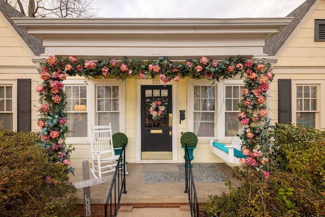 doorway to property with covered porch and a shingled roof