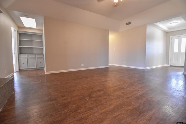 spare room with dark wood-type flooring, a raised ceiling, a skylight, ceiling fan, and built in features