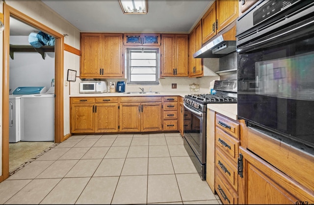 kitchen with light tile patterned floors, sink, black appliances, and washing machine and clothes dryer