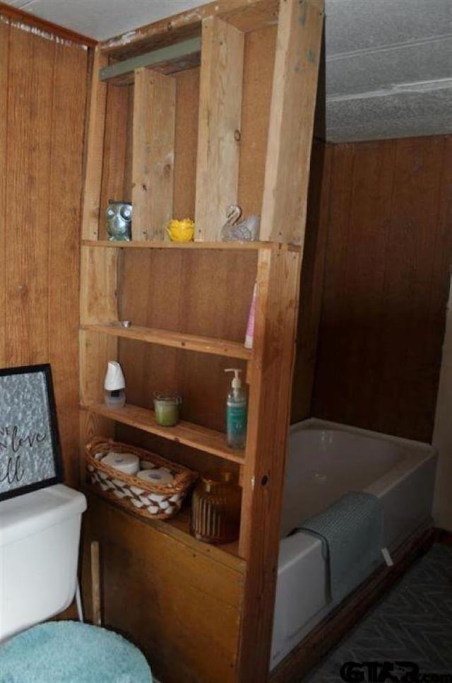 bathroom with toilet, a washtub, and wood walls