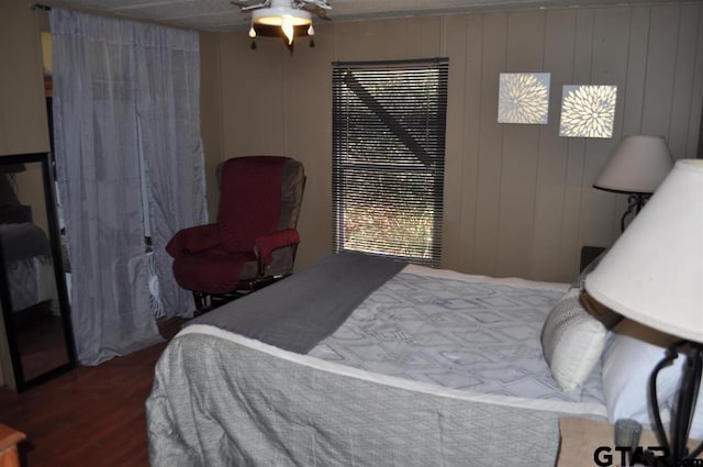 bedroom with wood-type flooring, wooden walls, and ceiling fan