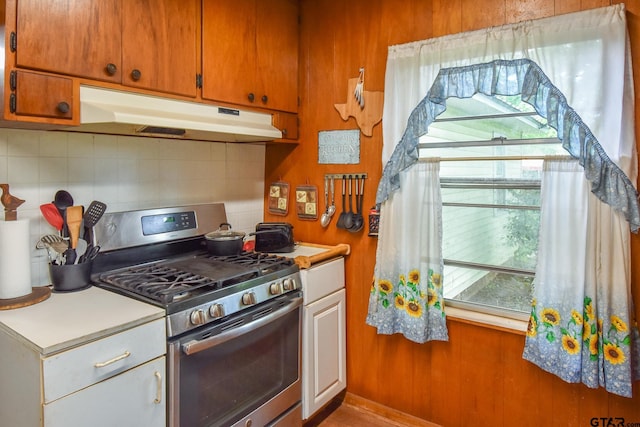 kitchen featuring light countertops, decorative backsplash, under cabinet range hood, and stainless steel range with gas cooktop