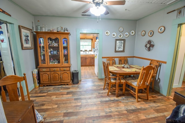 dining room featuring a ceiling fan, visible vents, wood finished floors, baseboards, and ornamental molding
