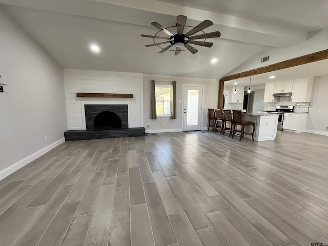 unfurnished living room with a large fireplace, ceiling fan, light hardwood / wood-style floors, and lofted ceiling with beams