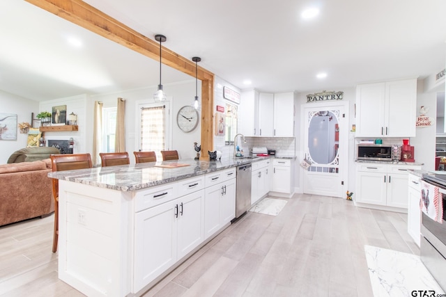 kitchen with a breakfast bar area, appliances with stainless steel finishes, white cabinetry, decorative light fixtures, and tasteful backsplash