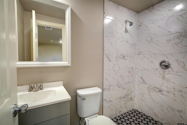 bathroom with a tile shower, vanity, and toilet