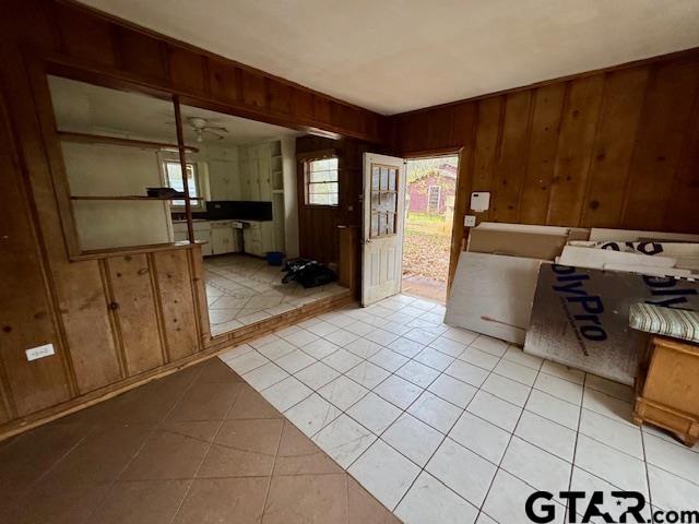 interior space with ceiling fan, light tile patterned floors, and wood walls