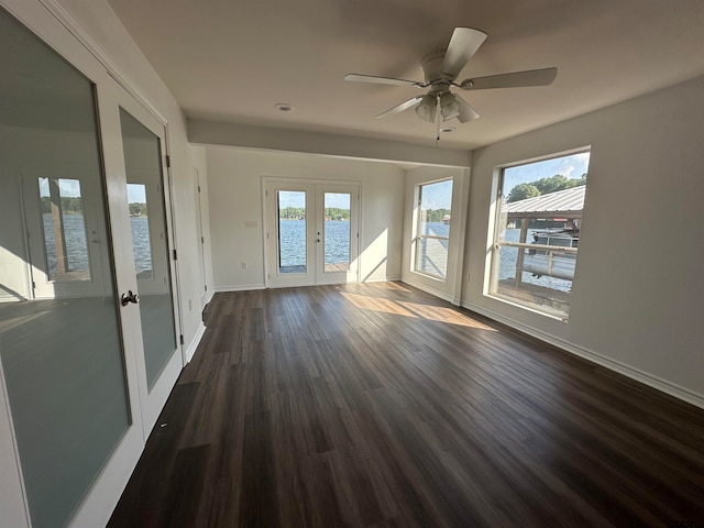 spare room with dark wood-type flooring, a healthy amount of sunlight, a water view, and french doors