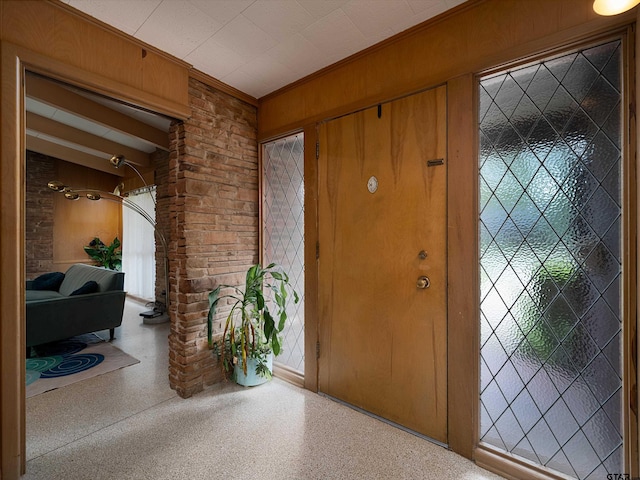 entrance foyer featuring wood walls, beam ceiling, and crown molding