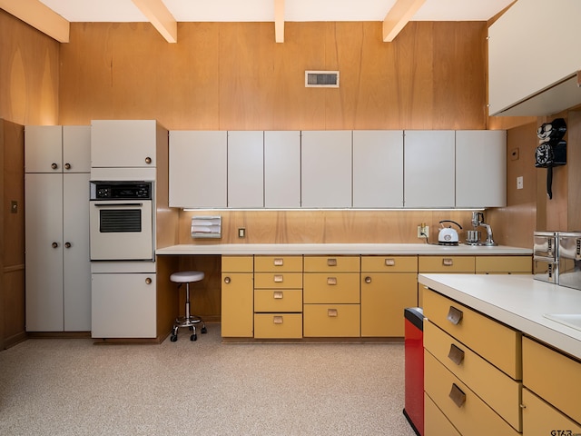 kitchen featuring white oven, beamed ceiling, and white cabinets