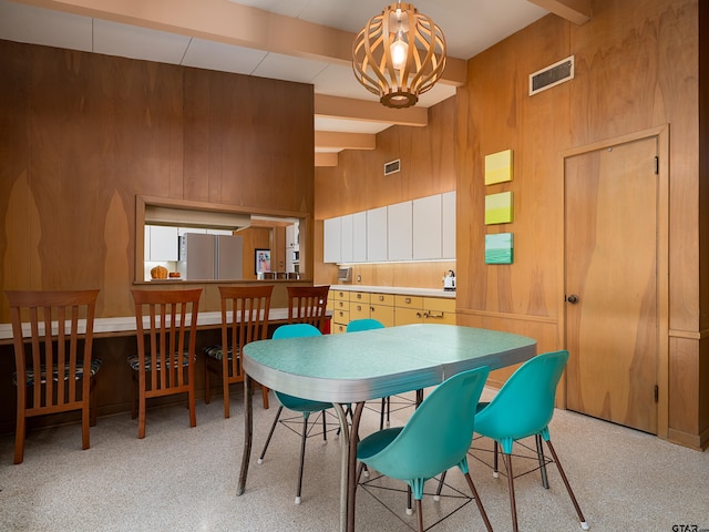 dining area with wooden walls, a chandelier, a towering ceiling, and beam ceiling