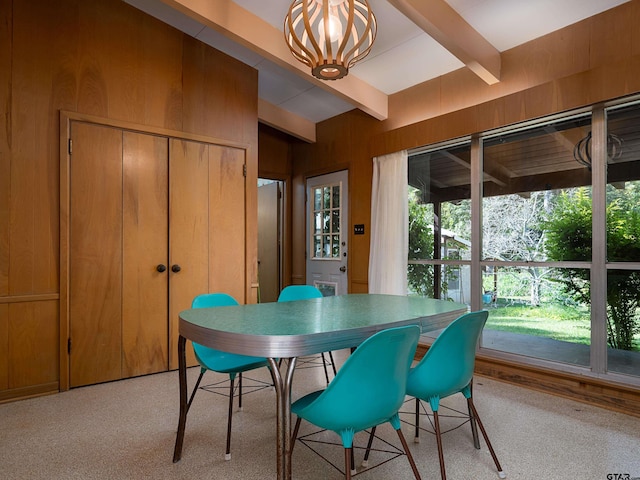 carpeted dining area featuring wood walls, a chandelier, and beam ceiling