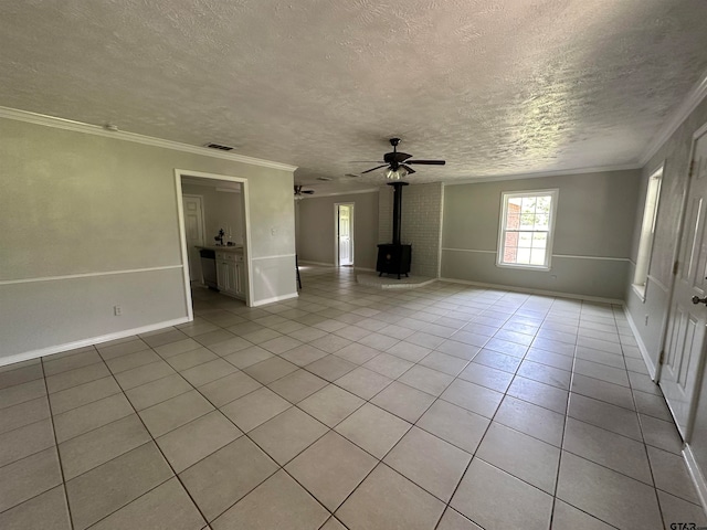 tiled empty room with a wood stove, a textured ceiling, crown molding, and ceiling fan