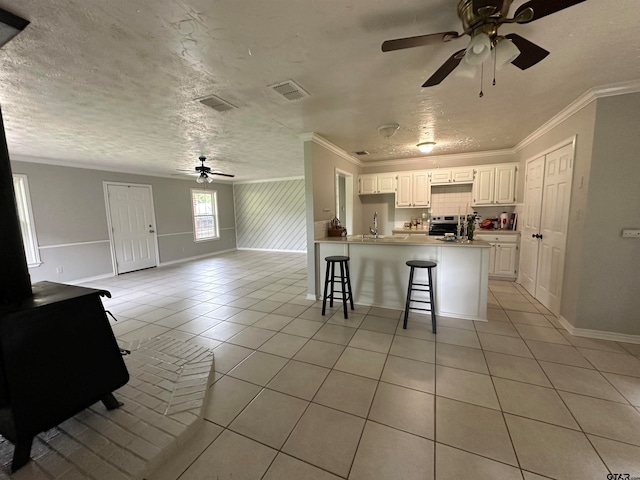 kitchen with kitchen peninsula, a textured ceiling, a breakfast bar area, light tile patterned flooring, and white cabinetry