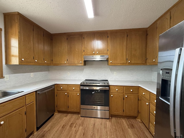 kitchen featuring tasteful backsplash, stainless steel appliances, a textured ceiling, and light wood-type flooring