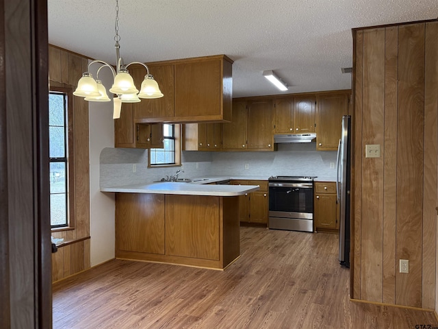 kitchen with pendant lighting, tasteful backsplash, kitchen peninsula, stainless steel appliances, and light hardwood / wood-style flooring