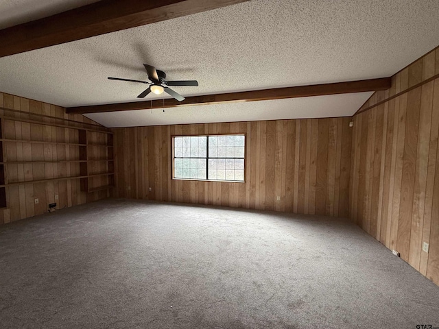 carpeted spare room featuring vaulted ceiling with beams, wooden walls, and a textured ceiling