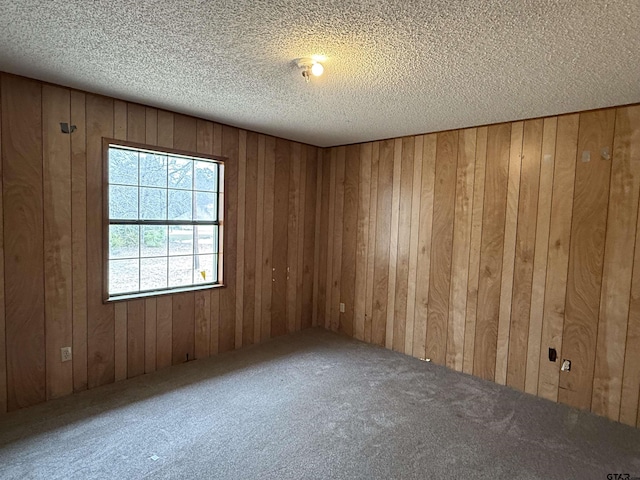 carpeted spare room featuring wooden walls and a textured ceiling