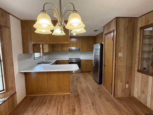 kitchen with sink, light wood-type flooring, appliances with stainless steel finishes, kitchen peninsula, and pendant lighting