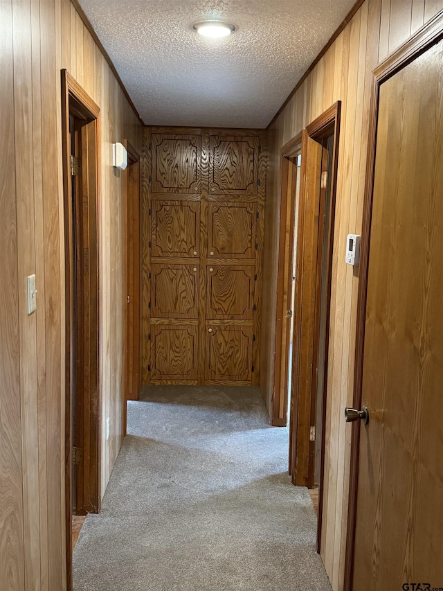 corridor with light carpet, ornamental molding, a textured ceiling, and wood walls