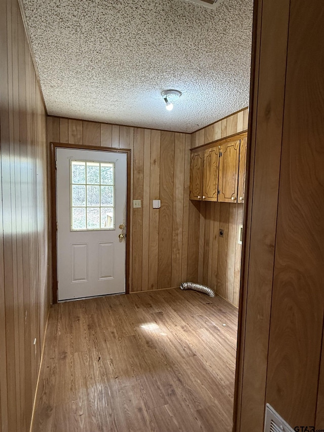 entryway with wooden walls, a textured ceiling, and light wood-type flooring