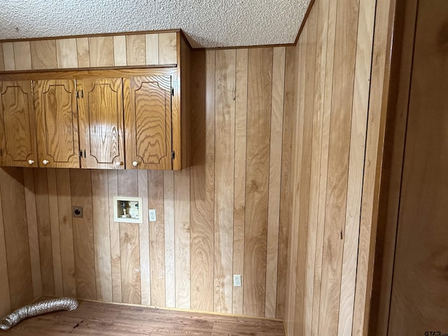 laundry area featuring electric dryer hookup, hookup for a washing machine, wooden walls, cabinets, and a textured ceiling