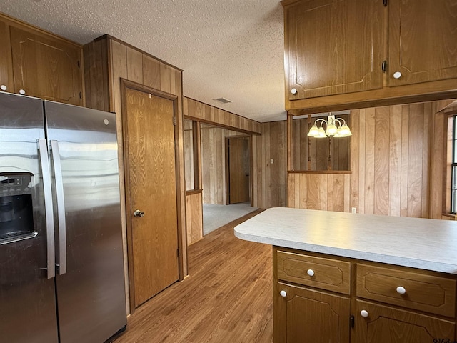 kitchen featuring light hardwood / wood-style floors, wood walls, a textured ceiling, and stainless steel refrigerator with ice dispenser